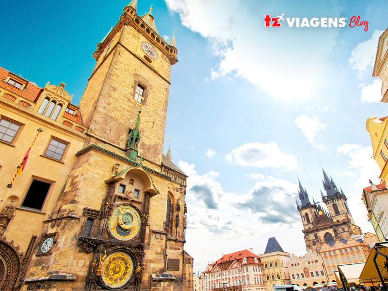 Um dos pontos turísticos de Praga mais visitados é o Orloj. Um relógio astronômico que fica na praça da cidade pequena. A imagem aparece o relógio, oldtown square de fundo e um céu azulado.
