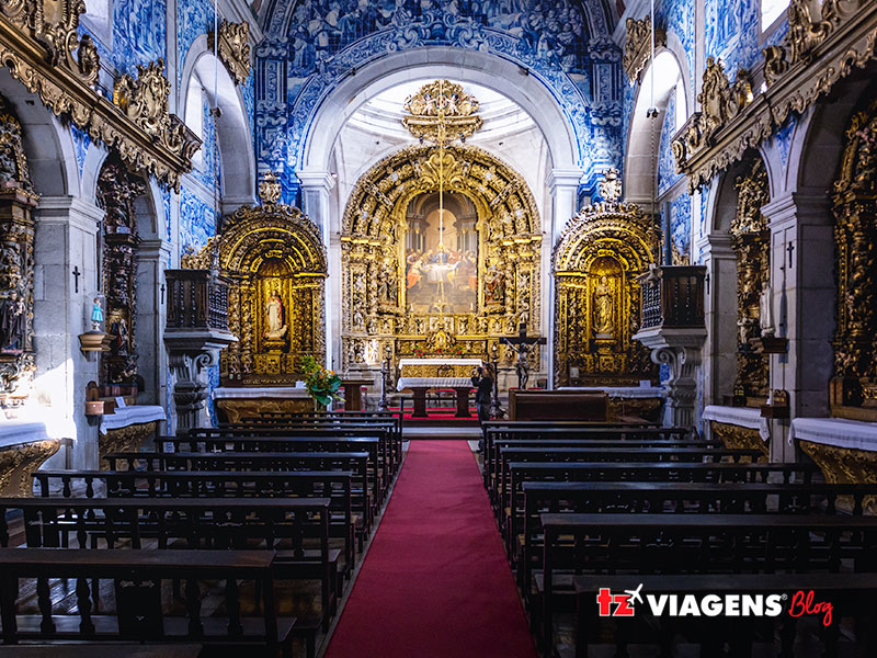 Viana do Castelo é um dos pontos do norte em uma Viagem para Portugal. Na imagem, intereiro da catedral, bancos da igreja, um tapete vermelho no meio e o altar ao fundo.